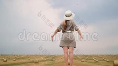 戴着帽子的漂亮年轻女子望着天空，双<strong>手举</strong>到麦田中央的天空上，挂着捆